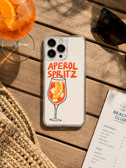 Phone case with Aperol Spritz design on a wooden table with a cocktail and menu.